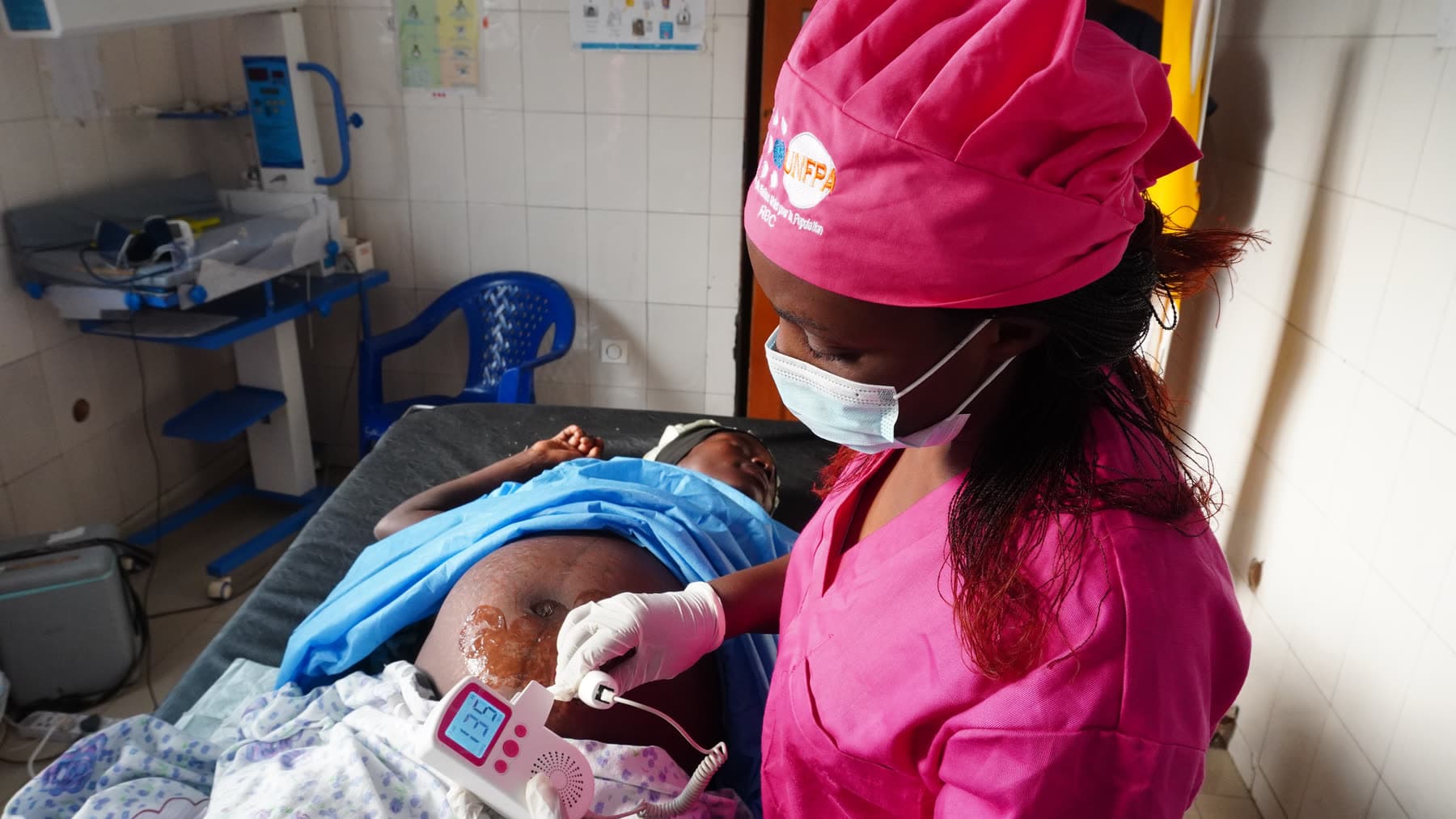 Un clinicien au chevet d'une patiente dans une maternité de RDC, tenant la tablette eGov qui fait tourner la plateforme